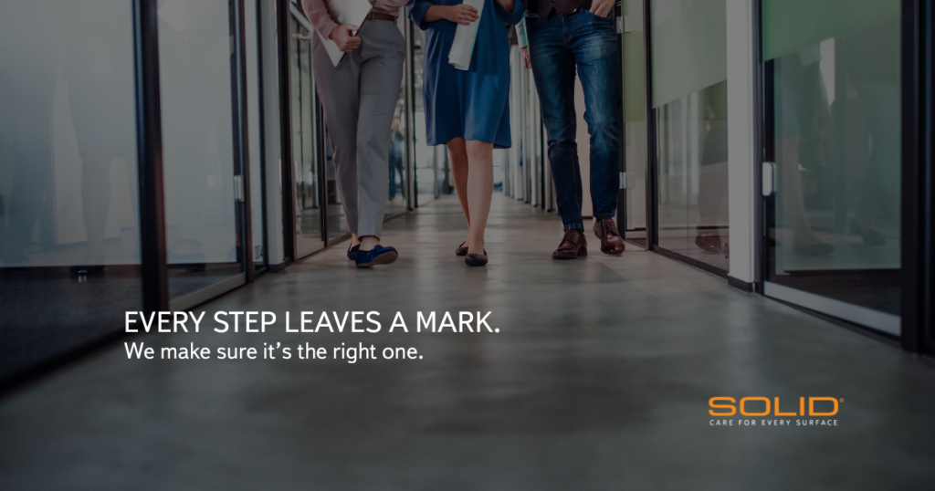 Three business professionals walking down a polished concrete corridor, shown from the waist down, highlighting foot traffic on commercial flooring