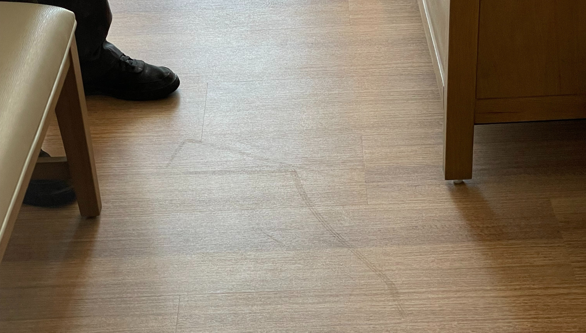 Person’s feet on scuffed and dull luxury vinyl tile flooring needing maintenance.