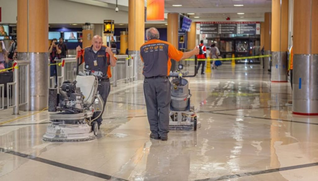 Two men in an airport polishing and cleaning the floors. 