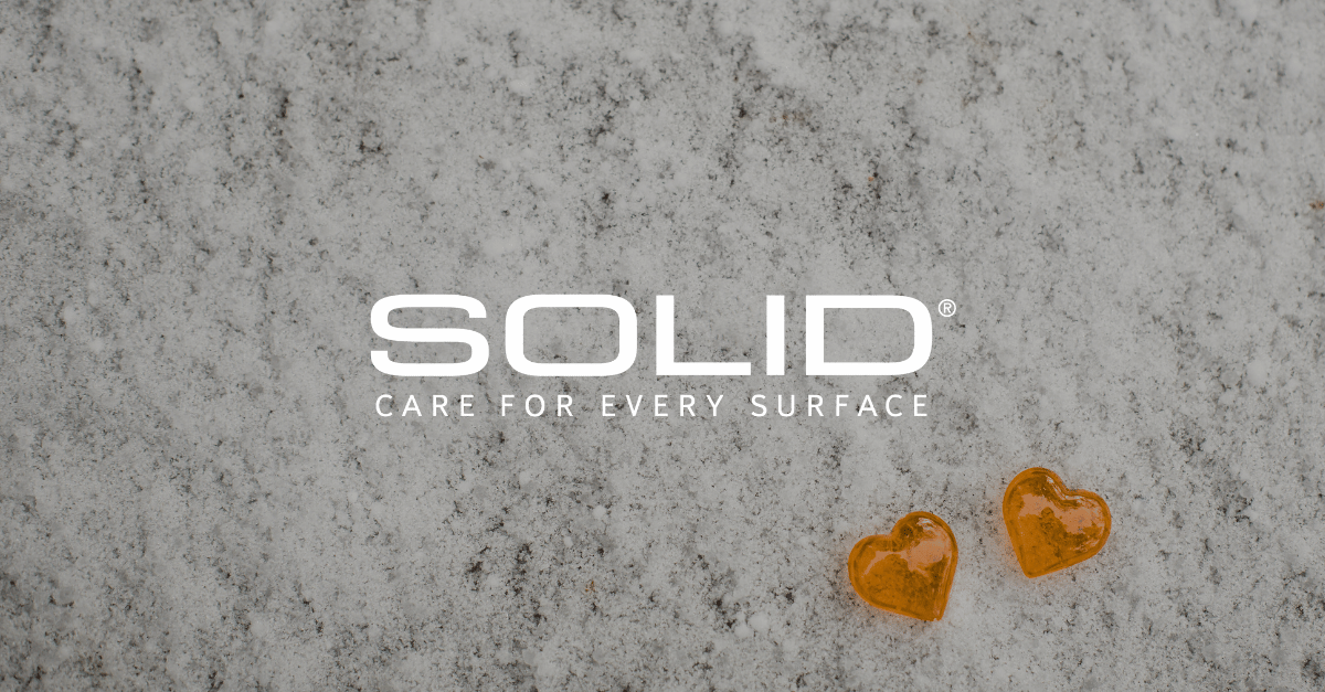 Two orange hearts on a polished granite floor with SOLID Surface Care logo in the corner, symbolizing care and attention to detail for Valentine’s Day.